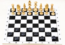 Playing By Different Rules On The Same Board - Black Checkers And White Chess Figures On Black White Chessboard, Chess Pieces And Checker Discs In Starting Positions (focus On Front Checkers)
