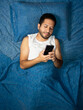 © Narayan - latin man using cell phone on blue bed, cell phone concept