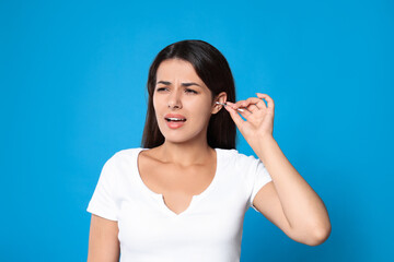 Sticker - Young woman cleaning ear with cotton swab on light blue background