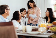 Happy Brazilian Multi-generation Family Having Breakfast Together And Talking At The Table. Extended Family Meeting The Newborn.