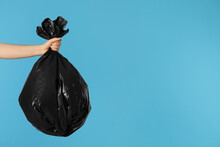 Woman Holding Trash Bag Full Of Garbage On Light Blue Background, Closeup. Space For Text