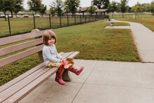 Young Girl Sits On Bench At Dog Park Holding Autumn Leaves