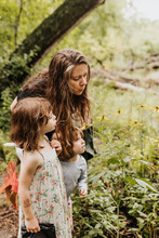 Mother And Daughters Look At Yellow Flowers Along Hiking Trail