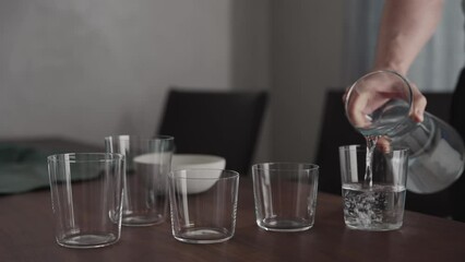 Wall Mural - Man pour water into glasses from carafe on walnut table