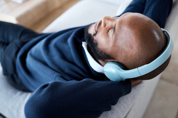 Poster - Music top view, headphones and black man on sofa in home living room streaming audio. Meditation, relax technology and male on couch in lounge listening to peaceful podcast, radio or sound in house.