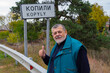 Portrait of positive UkrinianSenior standing on highway Kharkiv-poltava new sign marking Kopyly village, Ukraine