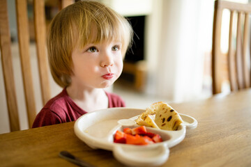 Wall Mural - Cute little toddler boy eating pancakes and strawberries at home. Fresh organic frutis for infants.