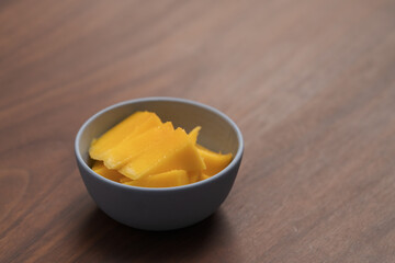 Wall Mural - Fresh sliced mango in a ceramic bowl on walnut table