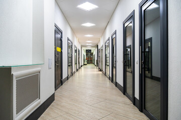  A corridor in an urban-type office building. Modern interior of the lobby of an office building with glass doors and clean white walls. A lighted long corridor in a modern business center.