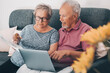 One old senior couple at home paying bills online with web banking app and checking the amounts on documents. Elderly and modern technology real life. Mature man and woman using computer and internet