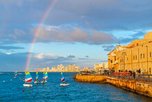 A Rainbow Appears Above The Skyline Of Tel Aviv, Seen From The Old Town Harbor Of The Historic Ancient City Of Jaffa, Israel Above A Children's Sailing Class At Sunset.	