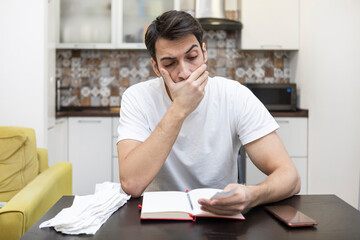 Close up of unhappy man sitting at the table, stressed and confused by calculate expense from invoice or bills, have no money to pay mortgage or loan. High prices and spending money concept