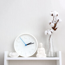 Buddha Figurine, Clock, Lotus Candlestick And Vase With Branch Of Cotton On White Shelf. Minimalistic Scandinavian Interior. Orientation Square. Selective Focus, Copy Space