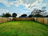 Fototapeta  - Large suburban backyard with a rustic wood fence, trimmed grass, and a concrete slab, set against neighboring homes under a clear blue sky.	