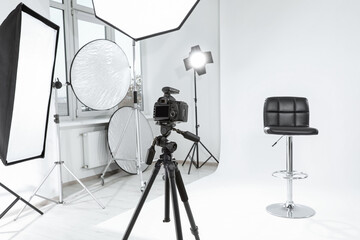 Sticker - Tripod with camera, bar stool and professional lighting equipment in modern photo studio