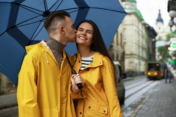 Sticker - Lovely young couple with umbrella kissing under rain on city street