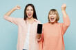 © ViDi Studio - Elder parent mom with young adult daughter two women together wear casual clothes hold use mobile cell phone blank screen area do winner gesture isolated on plain blue background. Family day concept.