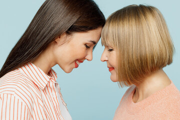 Close up side view lovely adorable caucasian elder parent mom with young adult daughter two women together in casual clothes touch forehead isolated on plain blue cyan background. Family day concept