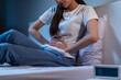 Flatulence ulcer, asian young woman hand on belly, stomach ache from food poisoning, abdominal pain and digestive problem, gastritis or diarrhoea sitting in bed room in the night. Abdomen inflammation