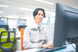 © HML - 作業着を着てパソコン作業をする若いエンジニアの男性