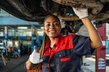 Engineer team checking under car condition on lifter in garage.Young auto mechanic in uniform is looking at camera and smiling examining car.