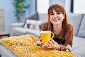 Poster - Young woman drinking coffee lying on sofa at home