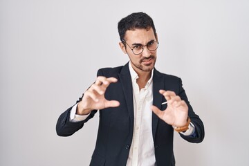 Wall Mural - Handsome business hispanic man standing over white background smiling funny doing claw gesture as cat, aggressive and sexy expression