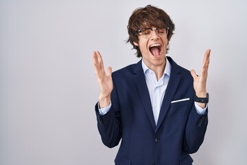 Poster - Hispanic business young man wearing glasses celebrating mad and crazy for success with arms raised and closed eyes screaming excited. winner concept