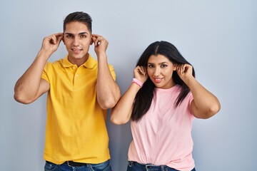 Poster - Young couple standing over isolated background smiling pulling ears with fingers, funny gesture. audition problem