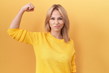 Poster - Young caucasian woman wearing yellow sweater strong person showing arm muscle, confident and proud of power