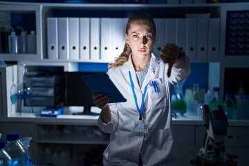 Poster - Beautiful blonde woman working at scientist laboratory late at night looking unhappy and angry showing rejection and negative with thumbs down gesture. bad expression.