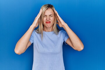 Wall Mural - Beautiful blonde woman wearing casual t shirt over blue background with hand on head for pain in head because stress. suffering migraine.