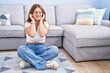 © Krakenimages.com - Young caucasian woman sitting on the floor at the living room covering ears with fingers with annoyed expression for the noise of loud music. deaf concept.