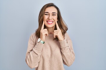 Poster - Young woman standing over isolated background smiling with open mouth, fingers pointing and forcing cheerful smile