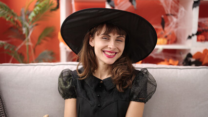 Poster - Young caucasian woman smiling wearing witch costume sitting on the sofa at home