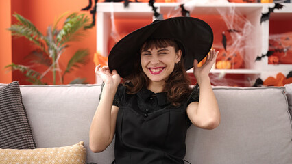 Sticker - Young caucasian woman smiling wearing witch costume sitting on the sofa at home