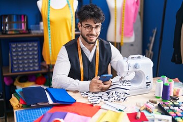 Canvas Print - Young hispanic man tailor smiling confident using smartphone at sewing studio