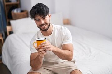 Sticker - Young hispanic man drinking cup of coffee sitting on bed at bedroom