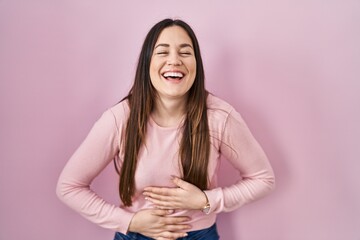 Poster - Young brunette woman standing over pink background smiling and laughing hard out loud because funny crazy joke with hands on body.