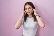 © Krakenimages.com - Young hispanic girl standing over pink background covering ears with fingers with annoyed expression for the noise of loud music. deaf concept.