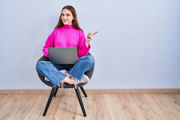 Poster - Young hispanic girl working using computer laptop with a big smile on face, pointing with hand finger to the side looking at the camera.