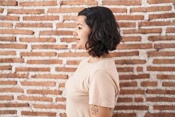 Canvas Print - Young hispanic woman standing over bricks wall looking to side, relax profile pose with natural face and confident smile.