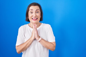 Sticker - Middle age hispanic woman standing over blue background praying with hands together asking for forgiveness smiling confident.