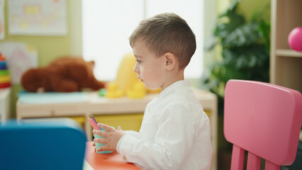 Poster - Adorable caucasian boy student sitting on table holding pencil at kindergarten