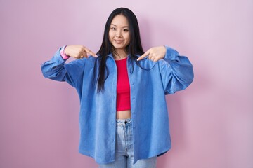 Poster - Young asian woman standing over pink background looking confident with smile on face, pointing oneself with fingers proud and happy.