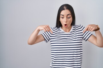 Poster - Young brunette woman wearing striped t shirt pointing down with fingers showing advertisement, surprised face and open mouth