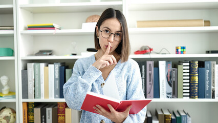 Poster - Young beautiful hispanic woman student reading book doing silence gesture at library university