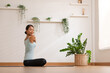 © 220 Selfmade studio - Fit and focused Asian woman practicing yoga in the comfort of her own home. Wearing comfortable clothing, she is performing various yoga poses in living room. Surrounded by natural light and peaceful