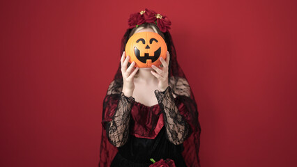 Wall Mural - Young blonde woman wearing katrina costume holding halloween pumpkin basket over face over isolated red background