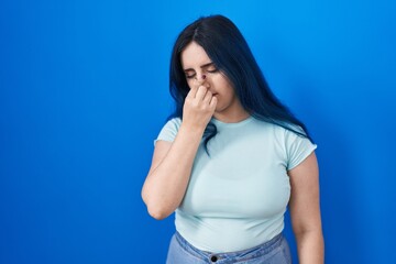 Sticker - Young modern girl with blue hair standing over blue background tired rubbing nose and eyes feeling fatigue and headache. stress and frustration concept.